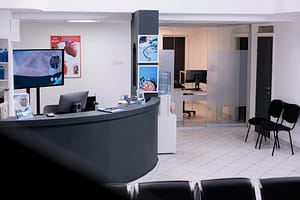 Small medical office reception area with curved desk, computer monitors, and private examination rooms in background