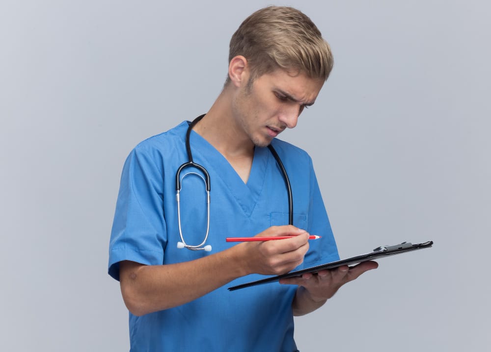 Healthcare professional in blue scrubs with stethoscope reviewing patient chart on clipboard